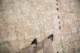 Distressed Oushak carpet pile with visible foundation, muted rose and beige colors. Feet on rug.