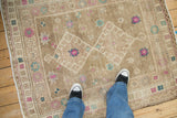 Distressed beige field of vintage Oushak rug with fuchsia and faded turquoise floral motifs.