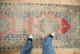 Distressed Oushak runner's decorative scalloped medallion, showcasing faded rose and denim blue tones.