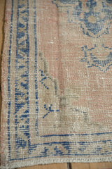 Distressed corner of vintage Oushak rug, showing worn dusty rose pile and blue geometric border.