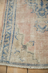 Distressed Oushak rug corner, with worn dusty rose, sky blue pile, and short fringe.