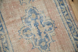 Distressed texture of vintage Oushak rug showcasing dusty rose field and sky blue floral pattern.