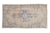 Vintage distressed Oushak rug with a cobalt blue floral medallion on a faded, dusty rose field.