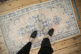 Styled view of a distressed vintage Oushak rug with dusty rose and blue tones, shown for scale.