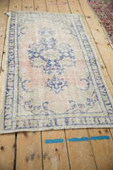 Angled view of a vintage distressed Oushak rug with a dusty rose and cobalt blue floral design.