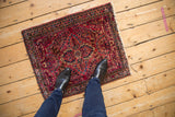 Overhead view of a vintage American Sarouk mat in cherry red and navy, shown for scale.