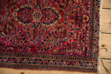 Corner of a fine Sarouk rug with intricate floral borders and visible tatter along the side.