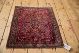 Angled overhead view of a vintage Sarouk rug with a dense millefleur design and worn edges.