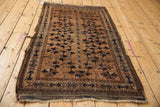 Antique Belouch rug showing worn side selvage, geometric border, and sand, navy tree patterns.