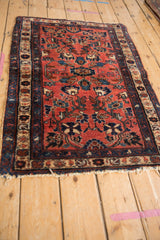 Angled view of the vintage Persian Mehreban rug, highlighting its raspberry field and worn, tattered edges.