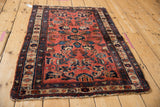 Angled view of a vintage Persian Mehreban rug with a raspberry floral field and tattered edges.