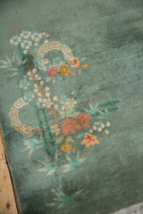 Diagonally oriented eucalyptus blossoms on sage green Chinese Nichols Art Deco rug pile, showing tatter.