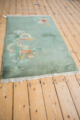 Art Deco rug with sage green open field, pale eucalyptus, blossoms, and tattered ends.