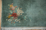 Corner of vintage Nichols Art Deco rug, showing sage green pile, colorful blossoms, and soft fringe.