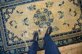Vintage Chinese Peking rug's cream field, showing significant pile wear and blue floral, bat motifs.