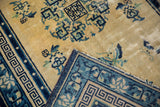 Peking rug corner folded, showing worn cream field, blue geometric border, and foundation.