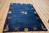 Navy blue border with beige floral branches, vase, and roundel motifs on a Peking rug.