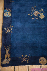Bottom corner of vintage Peking rug; navy border, beige vase, floral motif on cobalt field, tattered.