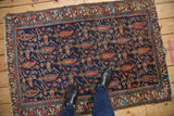 Navy field of a Mehreban rug with red paisley botehs, vinery, and tattered minor border.