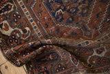 Folded corner of vintage Kamseh rug with terracotta, navy boteh border and visible foundation.