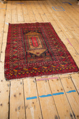 Vintage Afghan rug corner, cherry red, navy, and coffee brown tribal borders, frayed fringe.