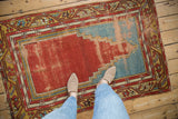 A person's view of a vintage Anatolian rug showing wear in its red and blue prayer design.
