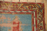 Corner of a vintage Anatolian rug showing worn pile, serpent borders, and tattered fringe.