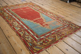 Angled view of a vintage Anatolian prayer rug showing its tattered edges and worn pile.