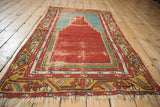 A distressed Anatolian prayer rug with a red stepped mehrab design, shown at an angle.