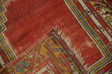 Folded corner of a vintage Anatolian rug with worn red pile, geometric borders, and short fringe.