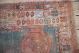 Antique Oushak rug detail: worn turquoise and coral border, pomegranate motifs, and tattered fringe.