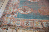 Corner of antique Oushak rug, with worn peach, turquoise border and tattered fringe.