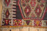 Geometric floral motifs in charcoal, red, and olive tones on a vintage Turkish Kilim.