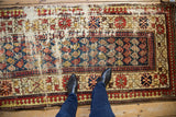 Feet on a vintage Caucasian runner, showing exposed foundation, cobalt blue, and red boteh patterns.