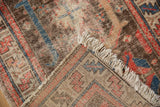 Vintage Hamadan rug folded to show worn pile, exposed foundation, and tattered fringe.