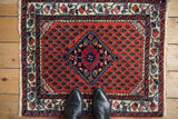Vintage Persian Engelas mat with a diamond medallion, shown for scale on a hardwood floor.