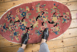 Dusty rose oval Art Deco rug with black dragon-like branches and colorful lotus blossoms.