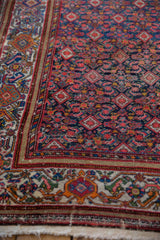 Angled detail of the vintage rug's intricate palmette border alongside its navy Herati field.