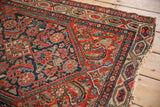Tattered corner of vintage Hamadan rug, revealing meandering vine border, red Herati motif.