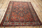 Worn vintage Hamadan rug corner, with red, navy, and green meandering border patterns.