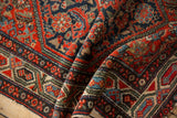 Meandering vine border, blossoms, and checkered flowers on folded vintage Hamadan rug with wear.