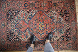 Vintage Farahan Sarouk rug, coral and navy medallion with palmettes, partially obscured by feet.