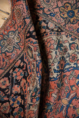 Textured close-up of vintage Farahan Sarouk rug with coral, navy, and ivory floral palmettes.