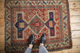 Antique Kazak rug's geometric border pattern in cherry red, navy blue, and beige with raw fringed edge.