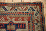 Antique Kazak rug corner with hand-knotted geometric borders in cherry red, navy, and ivory.