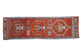 Distressed vintage Kurd runner with rust, orange, and charcoal geometric medallions containing human figures.