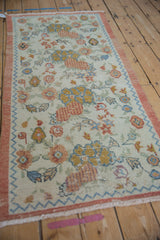 Distressed Oushak runner, ivory field with rust, blue floral bouquets and chevron border.