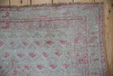 Distressed Oushak rug corner with worn pile texture, faint raspberry red pattern, and intact cording.