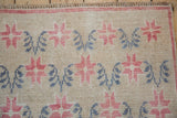 Texture of the distressed low pile with raspberry starbursts and dusty teal vines on an Oushak rug.