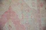 Evenly worn hand-knotted pile on a vintage Oushak showing pink and mint green decorative motifs.